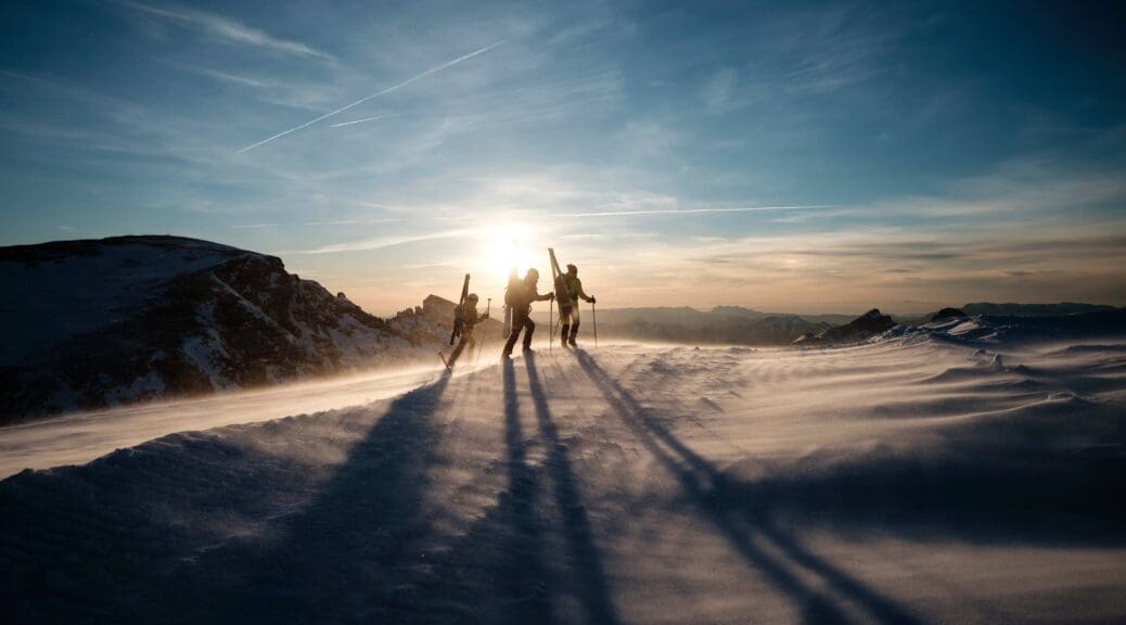 Three young adults skiing on a snowy mountain as the sun begins to go down