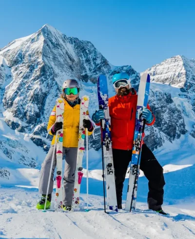 Two skiers holding their skis in front of a mountain in the Alps